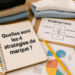 Carnet de notes ouvert avec la question Quelles sont les 4 stratégies de marque, entouré de graphiques marketing et d’outils de travail.